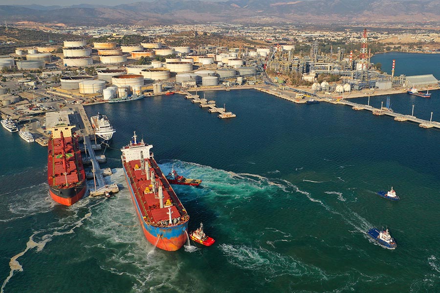Aerial photo of two large vessels docked in a port with an oil refinery
