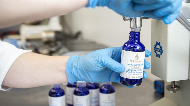 Person filling hand sanitizer product bottle in lab